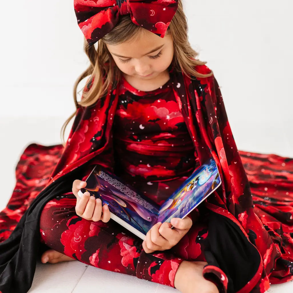 Child in a red and black outfit with a large bow, holding a colorful book.