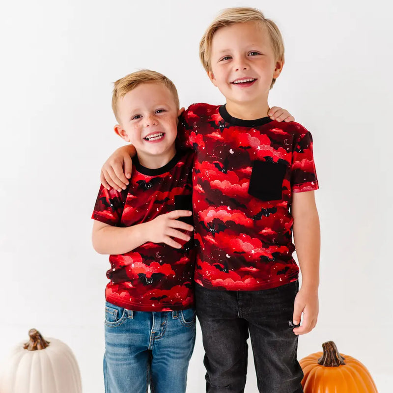 Two children wearing red and black patterned shirts standing next to pumpkins on a white background