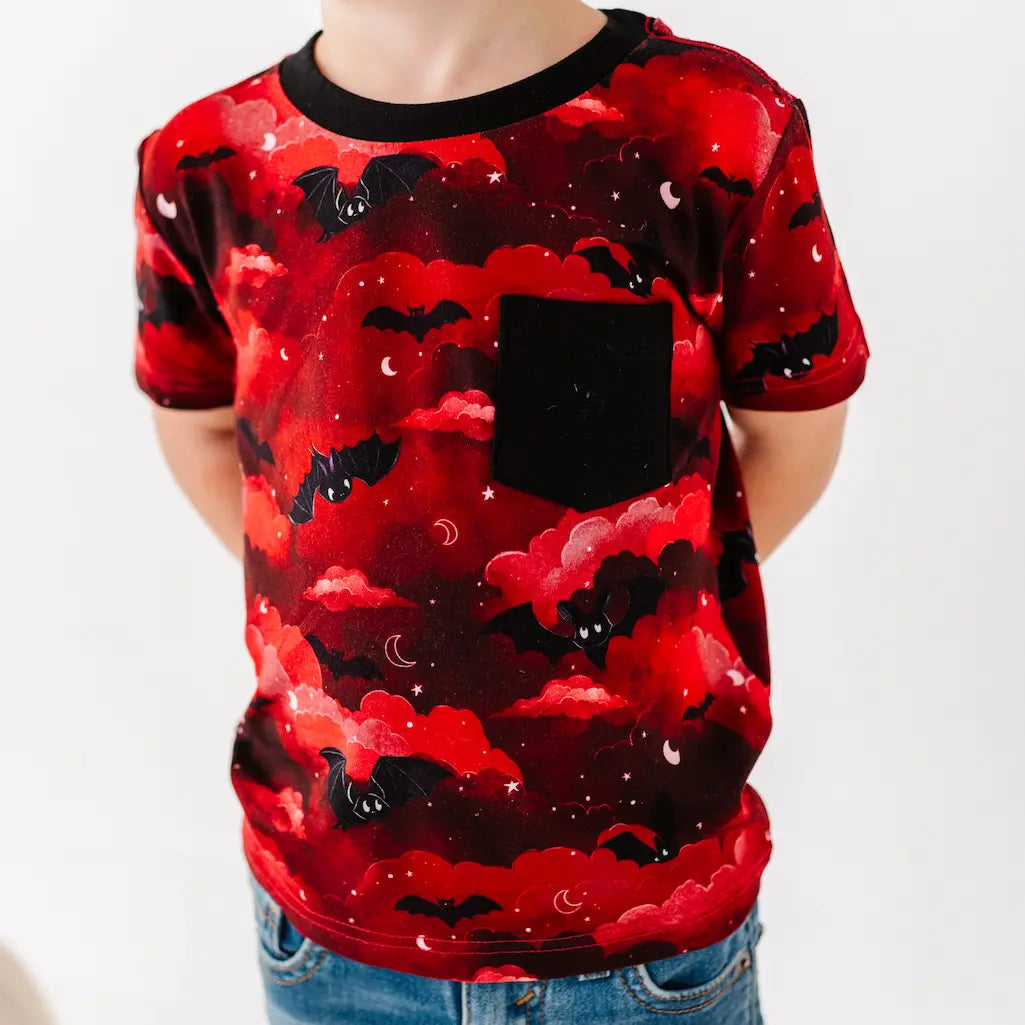 Red t-shirt with black bat pattern worn by a person on a white background