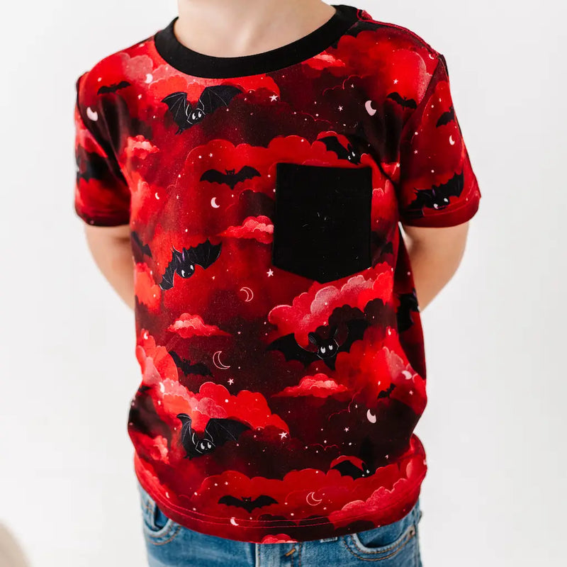 Red t-shirt with black bat pattern worn by a person on a white background