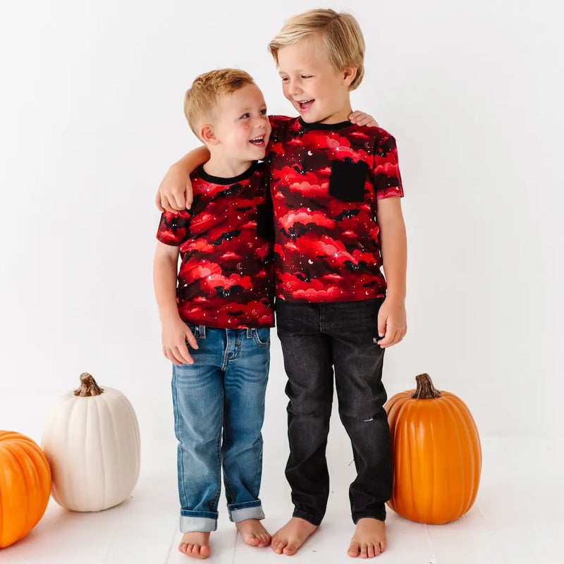 Two children wearing red and black patterned shirts with pumpkins around them on a white background