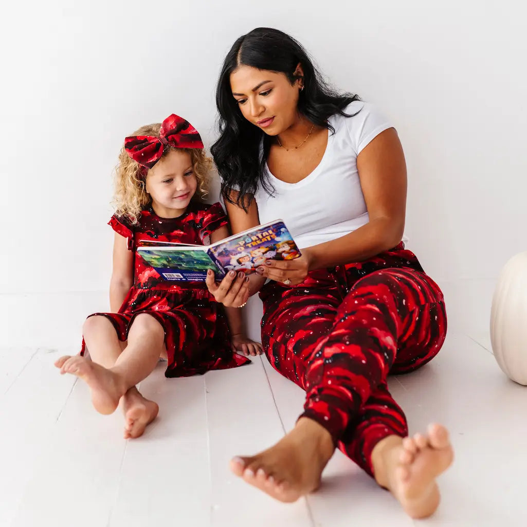 Woman and child in matching red and black outfits reading a book on a white floor.