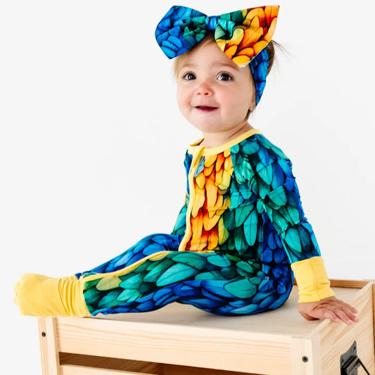 Baby in a colorful peacock costume sitting on a wooden stool.