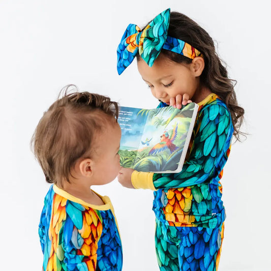 Two children in colorful dragon-themed outfits reading a book together on a white background