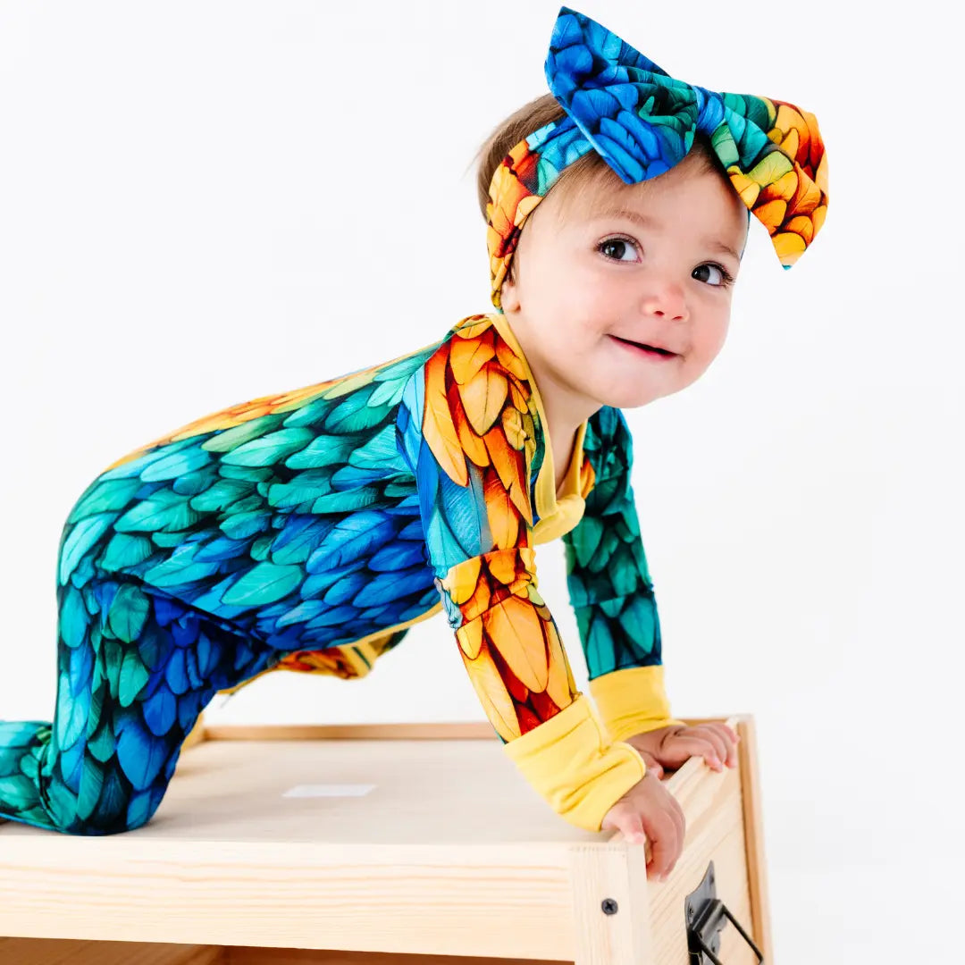 Child wearing a colorful dragon-themed onesie and headband on a white background