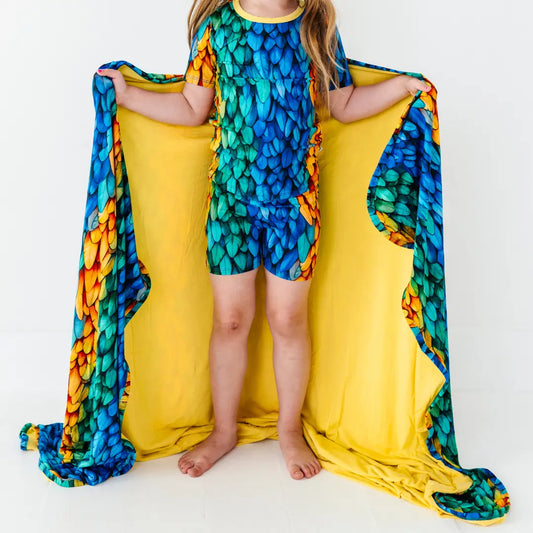 Child wearing a colorful dragon costume with a yellow blanket underneath on a white background