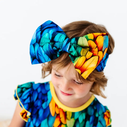 Child wearing a colorful outfit with large bow headbands on a white background