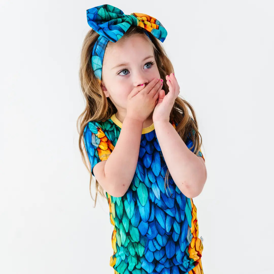 Child wearing a colorful dress with a dragon scale pattern and a matching headband.