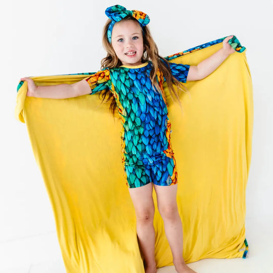 Young girl wearing a colorful dress with a yellow fabric draped over her shoulders on a white background