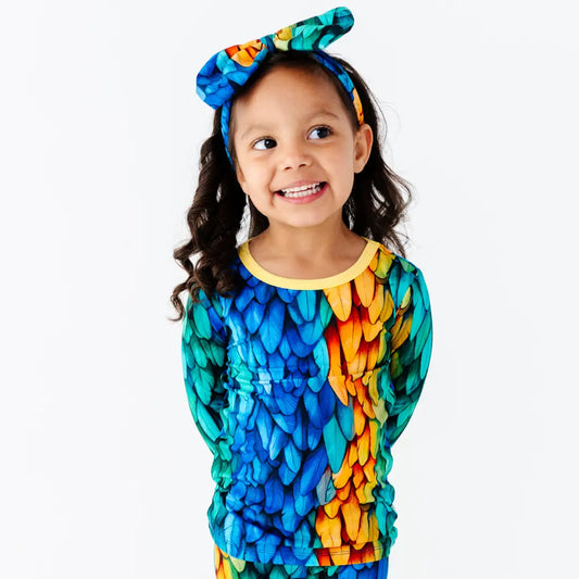 Child wearing a colorful shirt with a parrot pattern and a matching headband on a white background