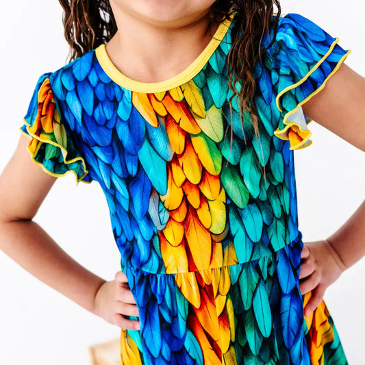 Child wearing a colorful dress with feather pattern on a white background