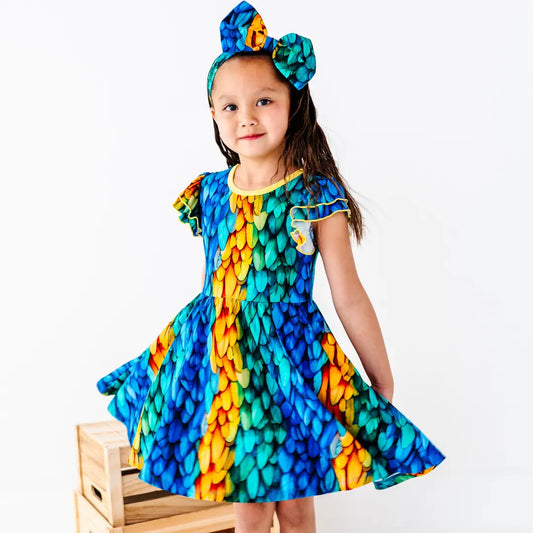 Young girl wearing a colorful dress with a pattern of blue, green, and orange on a white background.