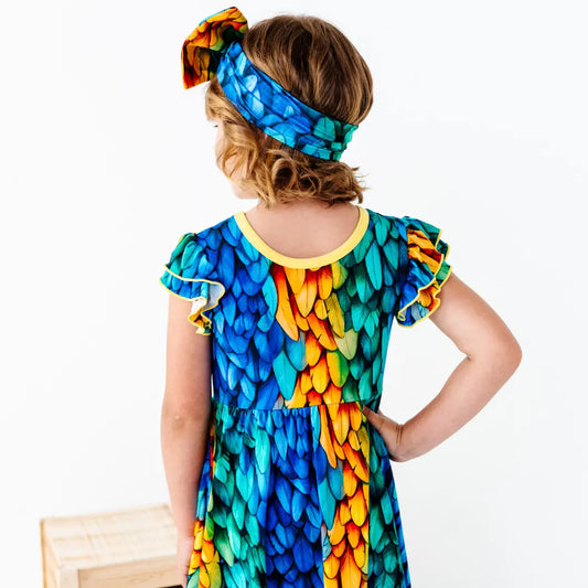 Child wearing a colorful parrot-themed dress and headband on a white background