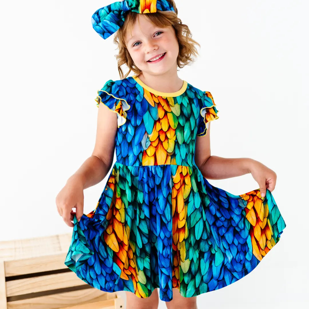 Child wearing a colorful dress with feather pattern on a white background