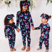 Three children holding hands in matching black butterfly print pajamas and bow headbands.