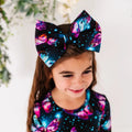 A child wearing a headband with a bow featuring a pattern of twinkling stars and shimmering wings in soft, pastel shades.
