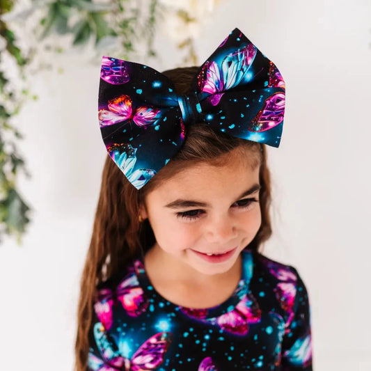 A child wearing a headband with a bow featuring a pattern of twinkling stars and shimmering wings in soft, pastel shades.
