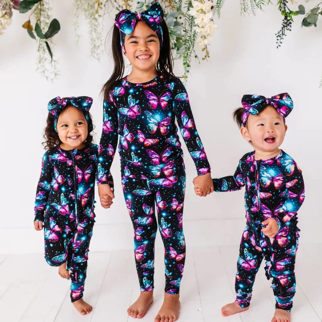Three children wearing matching two-piece pajama sets with a pattern of stars and shimmering wings in soft, pastel shades.