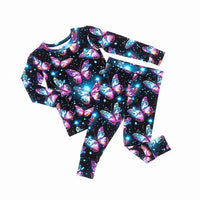 Flat lay of a two-piece pajama set with glowing pink and blue butterflies on black, on a white background.