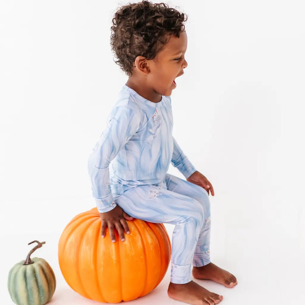 Child in blue pajamas sitting on a pumpkin with a white background