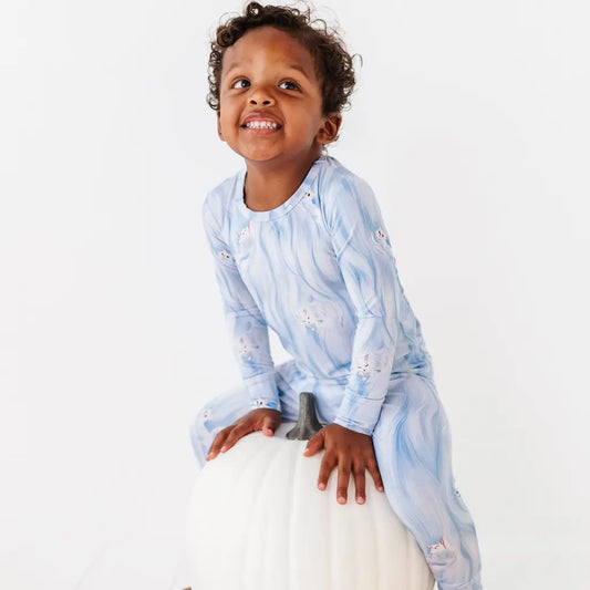 Child wearing a light blue patterned outfit sitting on a white pumpkin against a white background
