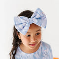 Child wearing a large blue bow headband with a white background