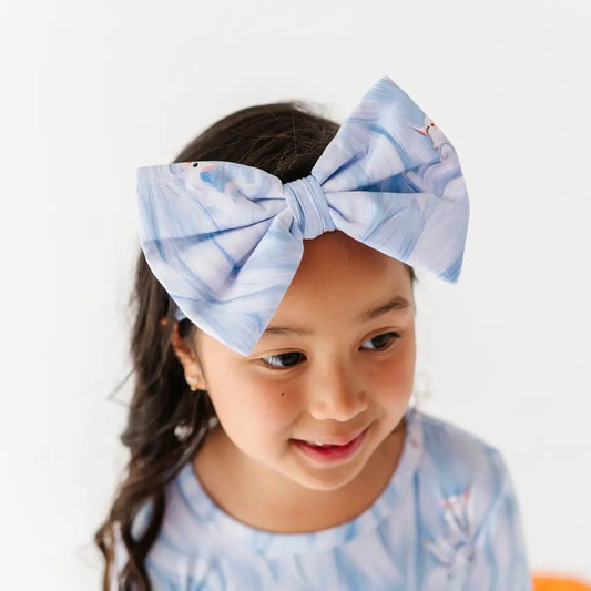 Child wearing a large blue bow headband with a white background