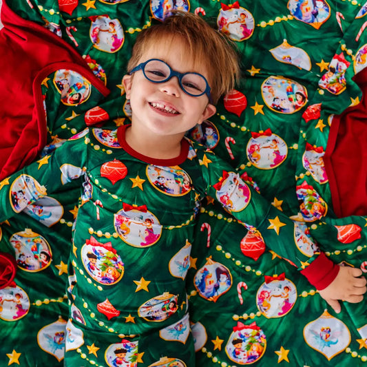 Child wearing a Christmas-themed pajama with cartoon characters, lying on a matching blanket.