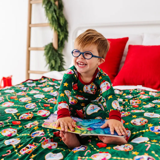Child in festive pajamas reading a book on a bed with Christmas decorations.