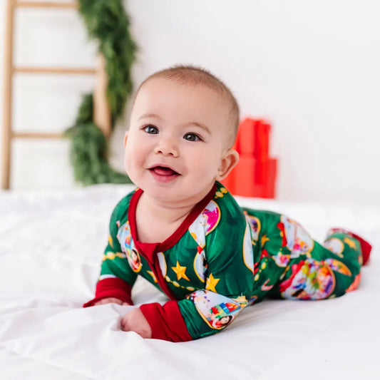 Baby wearing a festive onesie with Christmas-themed designs on a white blanket.