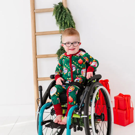 Child in a wheelchair wearing a festive onesie with Christmas-themed designs.