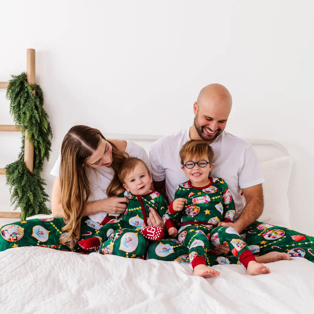 Family of four wearing matching Christmas pajamas sitting on a bed.