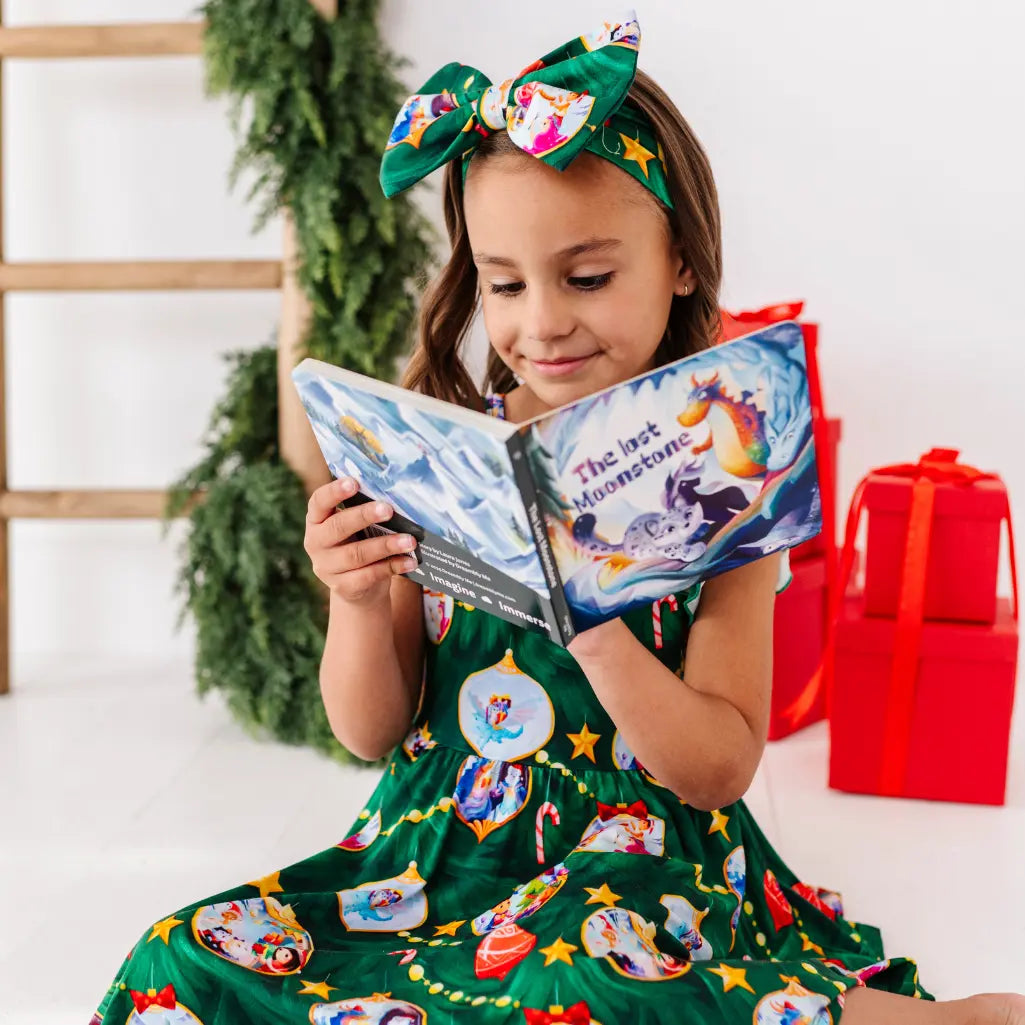 Young girl in a green dress with festive patterns, reading a book, wearing a matching headband.