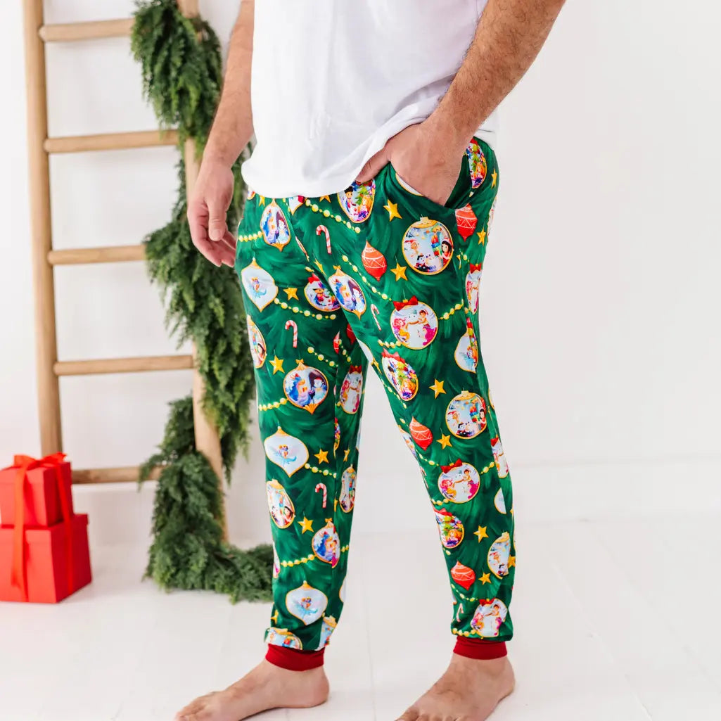 Person wearing festive green pajama pants with cartoon character pattern, standing against a white background with Christmas decorations.