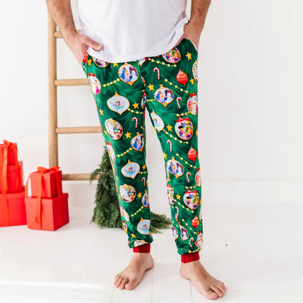Person wearing festive green pajama pants with Christmas-themed design, standing in a room with Christmas decorations.