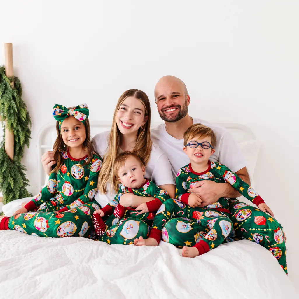 Family of four wearing matching Christmas pajamas on a bed.