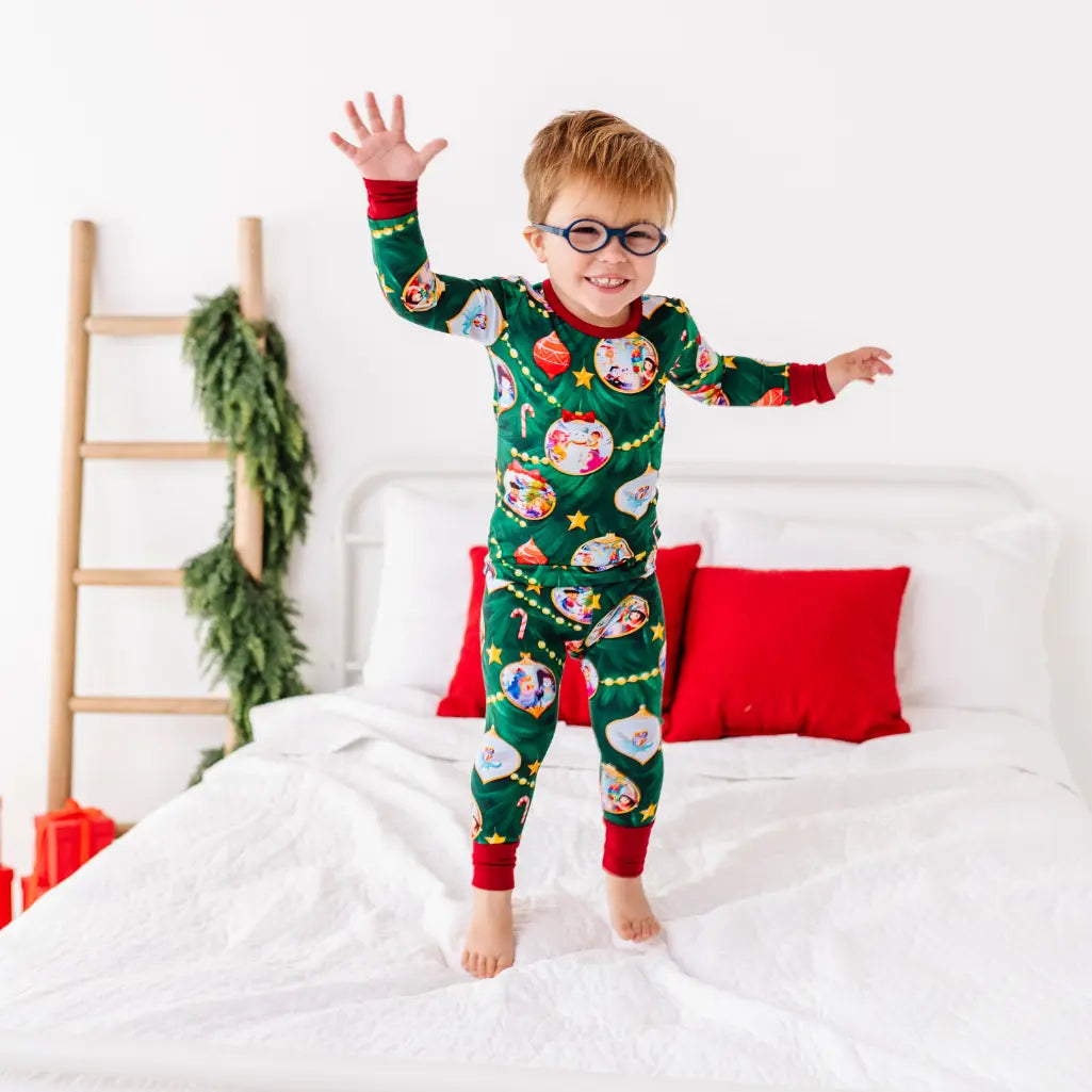 Child wearing festive pajamas with Christmas-themed design on a white bed.