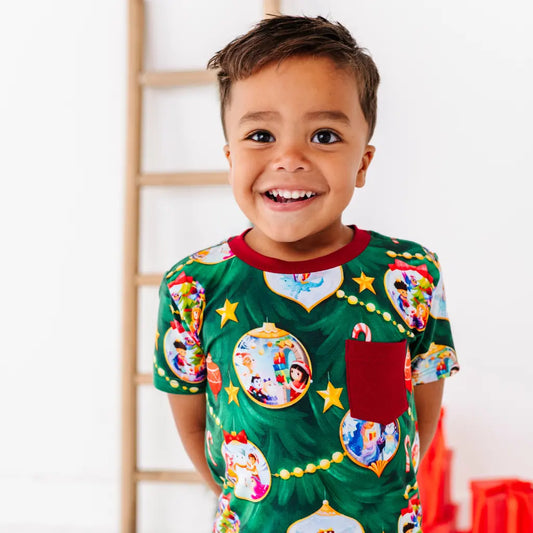 Child wearing a festive green pajama with colorful designs, standing against a white wall.