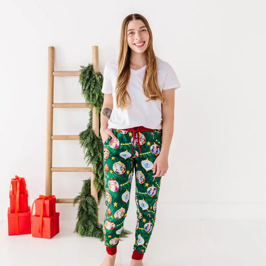 Woman wearing festive pajama pants with a white shirt, standing next to a wooden ladder and red gift boxes.