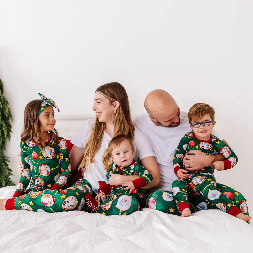 Family of five wearing matching green pajamas with festive designs on a white bed.