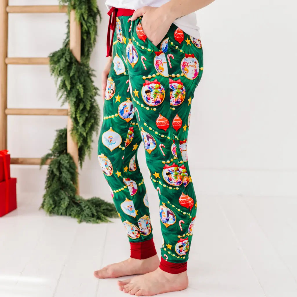 Person wearing festive green pajama pants with Christmas-themed decorations on a white background.