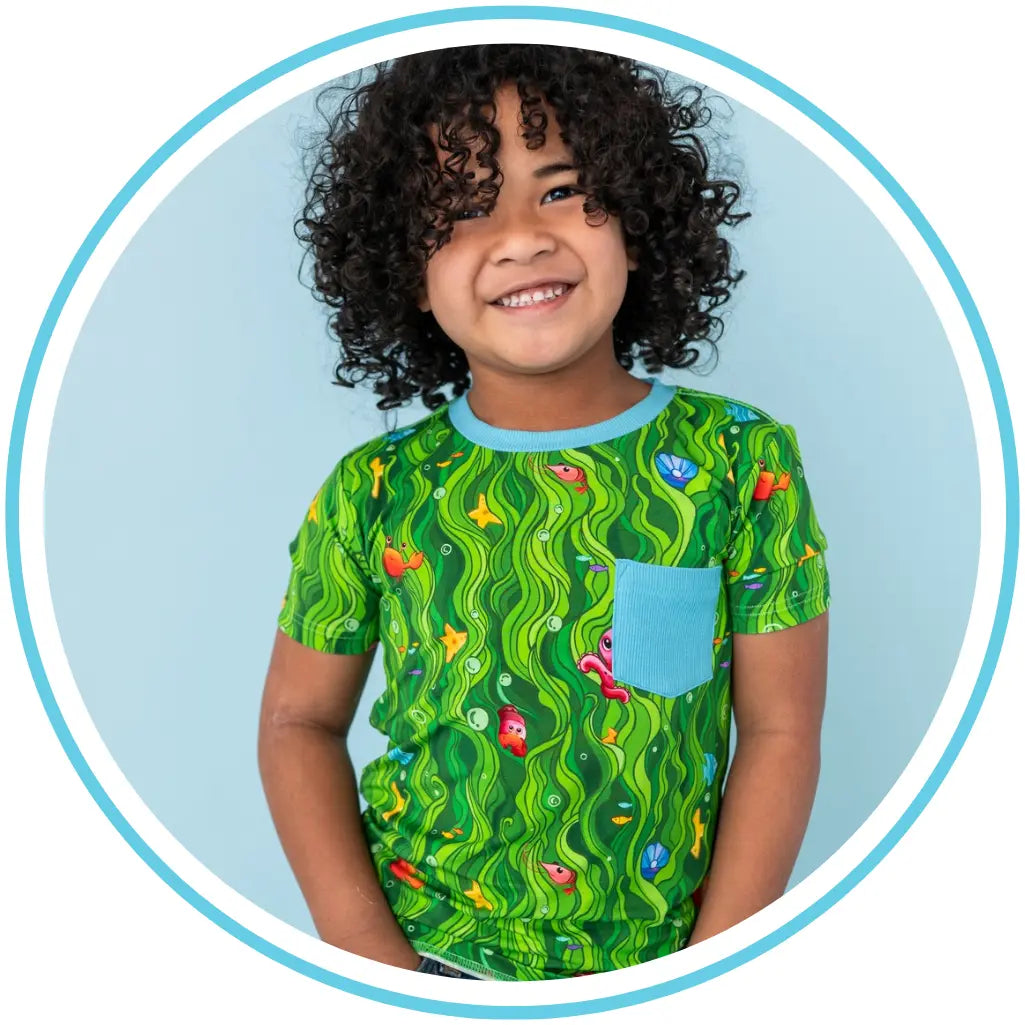 Child wearing a green patterned shirt with a blue pocket on a light blue background