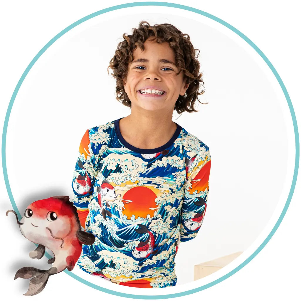 Child wearing a colorful shirt with a fish design, holding a plush toy, on a white background.