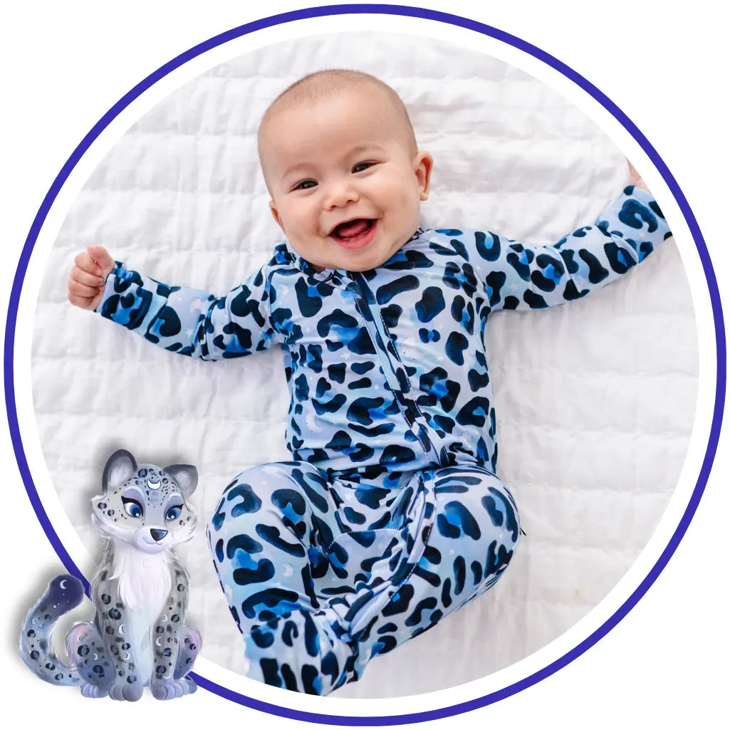 Baby wearing a blue leopard print onesie on a white blanket with a toy snow leopard.