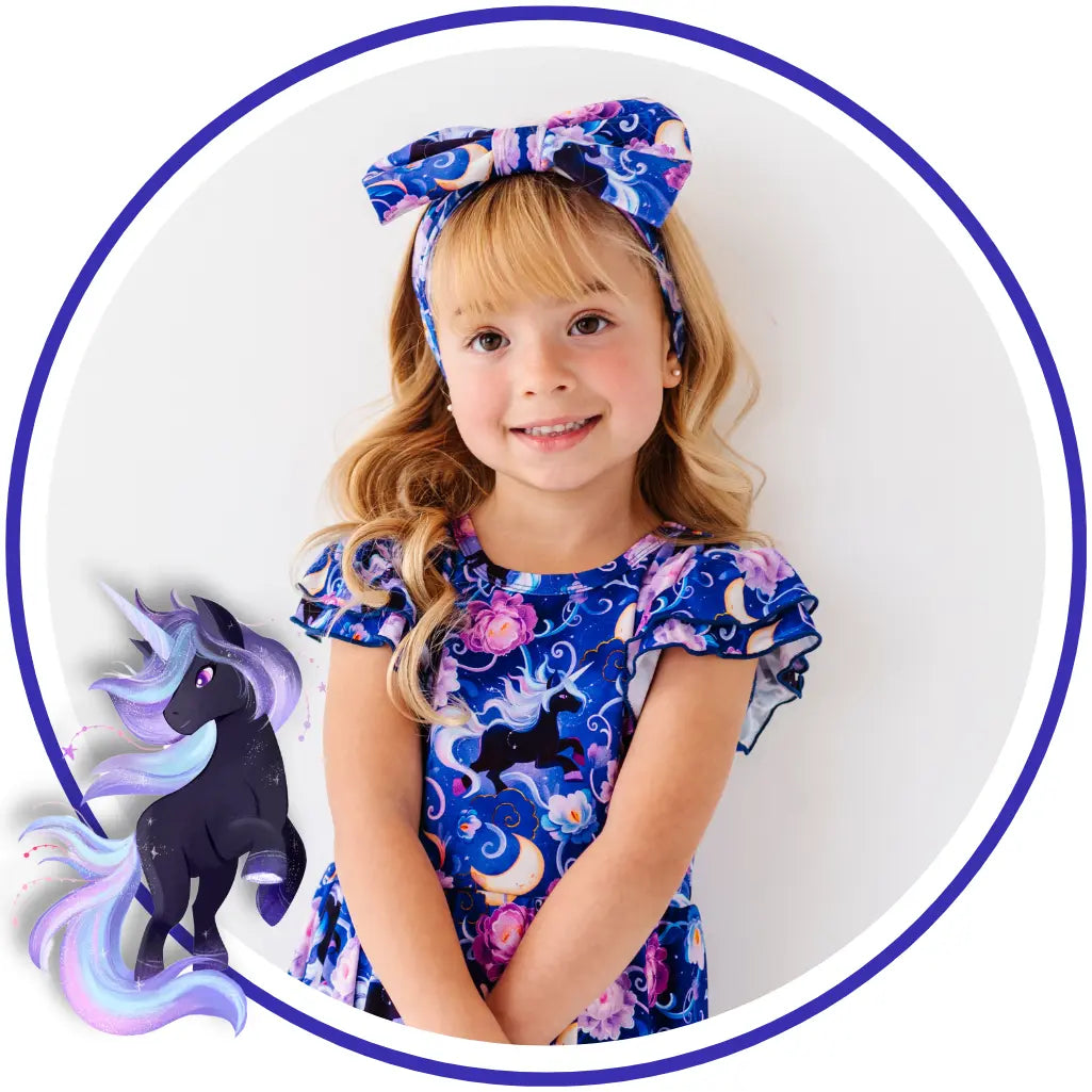 Young girl wearing a blue dress with unicorn design and matching headband on a white background