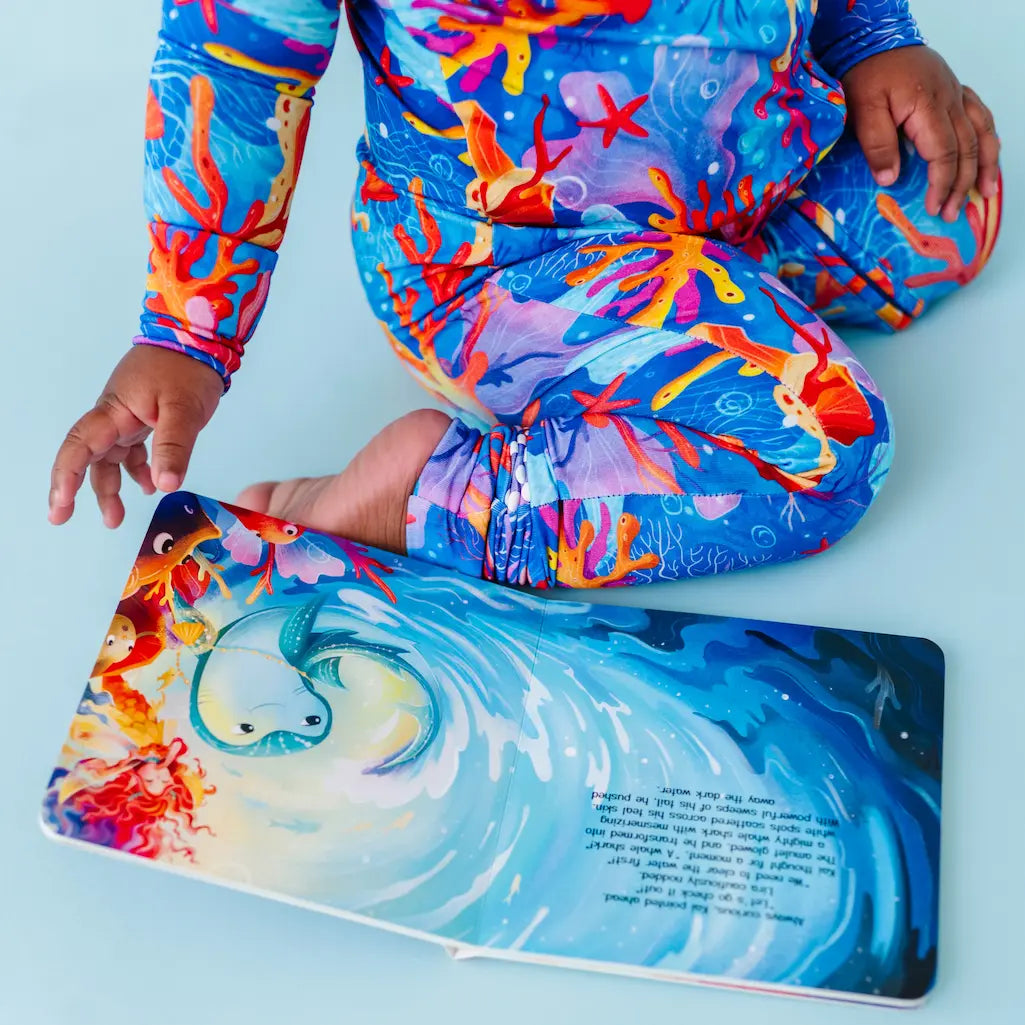 Child wearing colorful coral-themed swimsuit holding a matching swimsuit box on a blue background