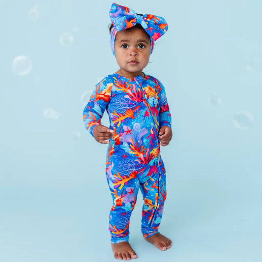 Child wearing a colorful coral reef-themed swimsuit and bow on a light blue background.