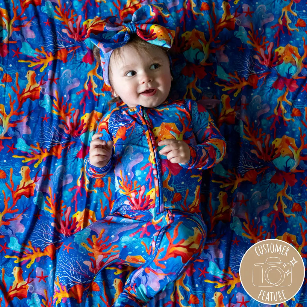 A baby wearing a colorful floral outfit with a bow on the head, lying on a matching floral blanket.