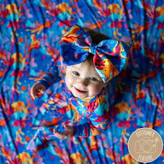 A baby wearing a colorful bow headband with a vibrant coral and sea life pattern.