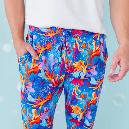 Colorful coral reef patterned pants worn by a person against a light blue background.